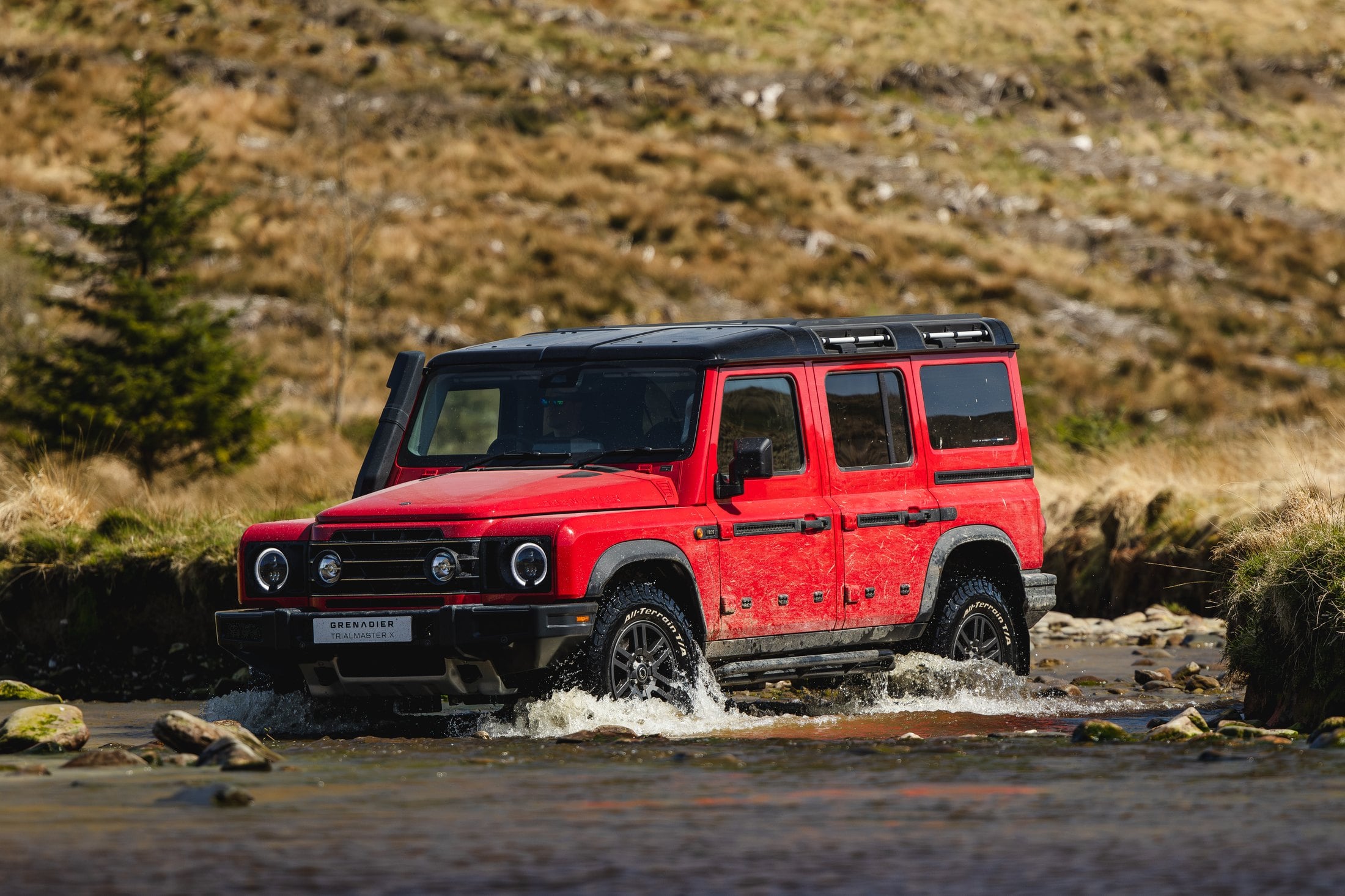 Official photo of the Devil Red INEOS Grenadier Trialmaster X wading a rocky stream
