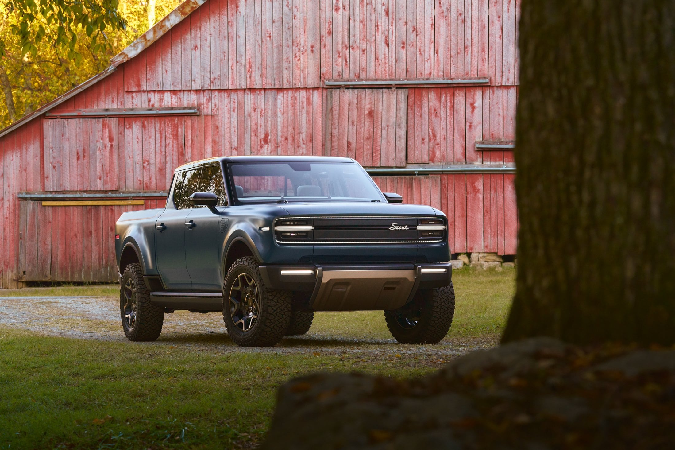 Official Scout Motors photo of the Terra pickup, front three-quarter in teal next to a red barn