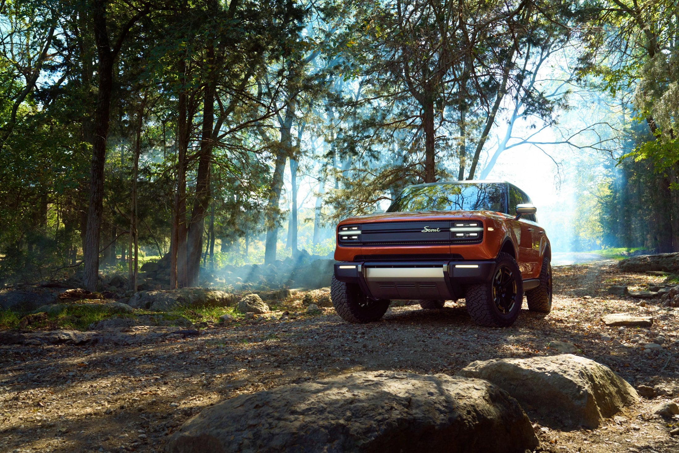 Official Scout Motors photo of the Traveler SUV, front three-quarter in burnt orange on a forest trail