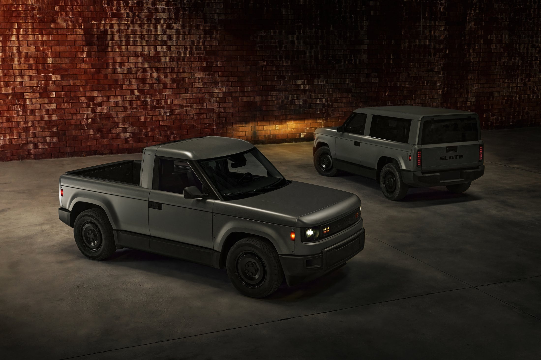 Official Slate photo of the two-seat pickup in front and the enclosed SUV behind, in a brick warehouse