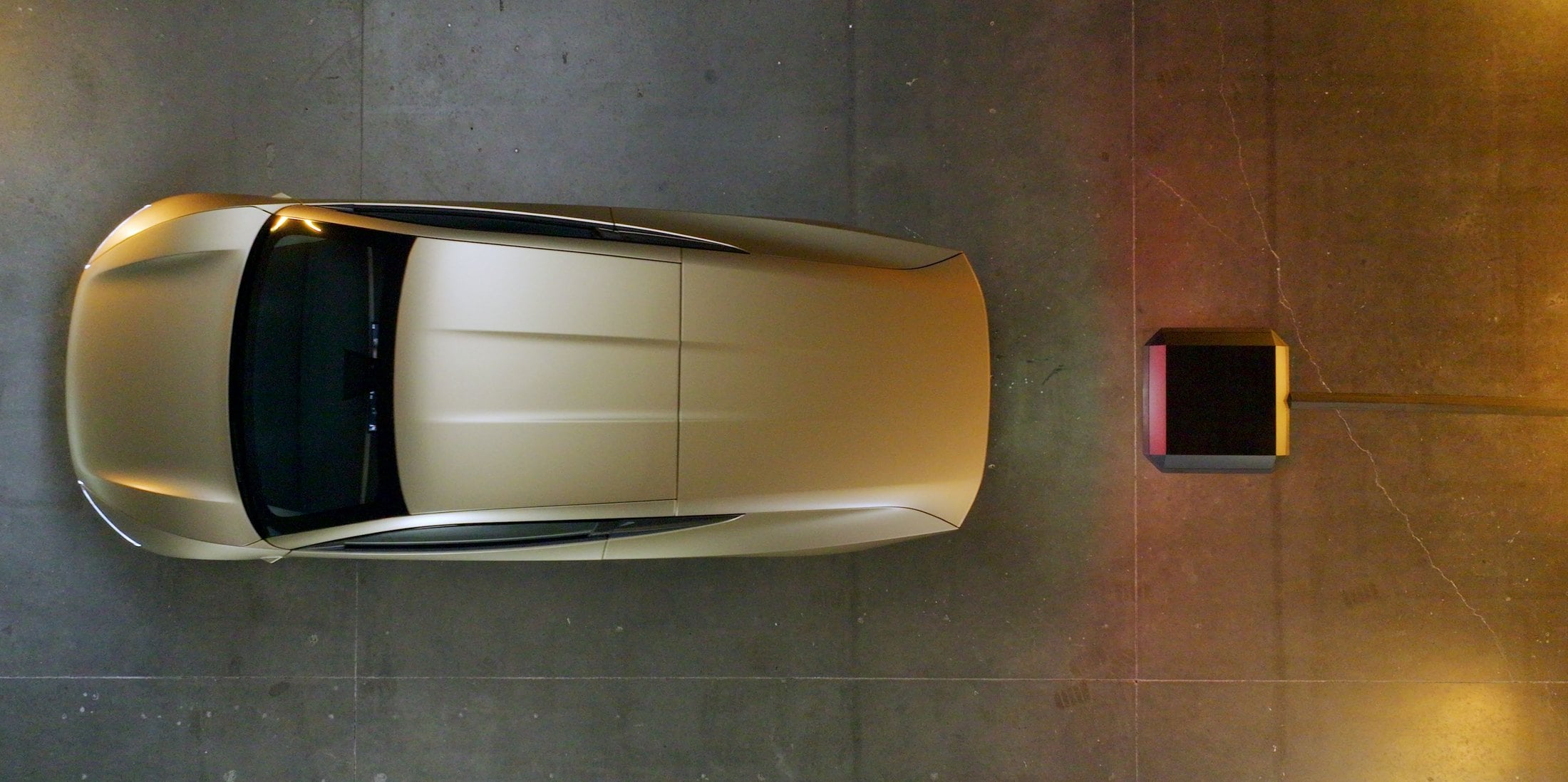 Overhead view of a gold Tesla Cybercab on concrete next to a wireless charging pad