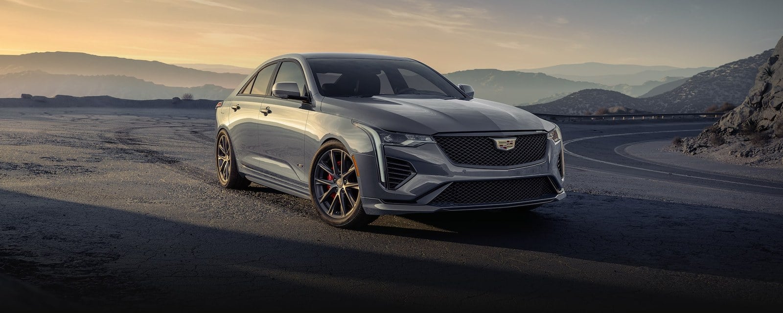 Official Cadillac photo of a gray 2026 CT4-V Blackwing front three-quarter on a mountain road at golden hour