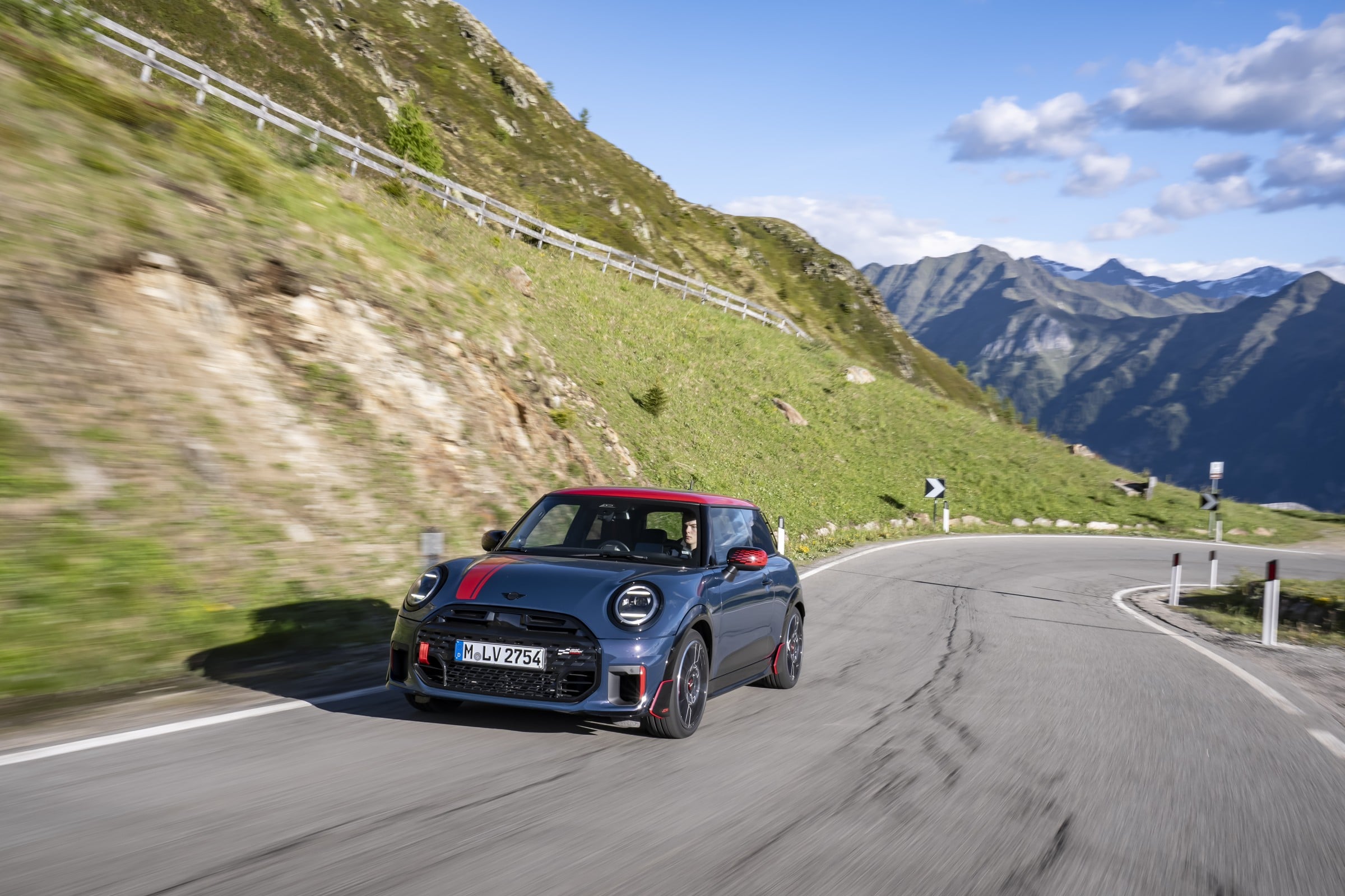Official MINI photo of a 2027 JCW 2 Door in Indigo Sunset Blue with red roof on a mountain road