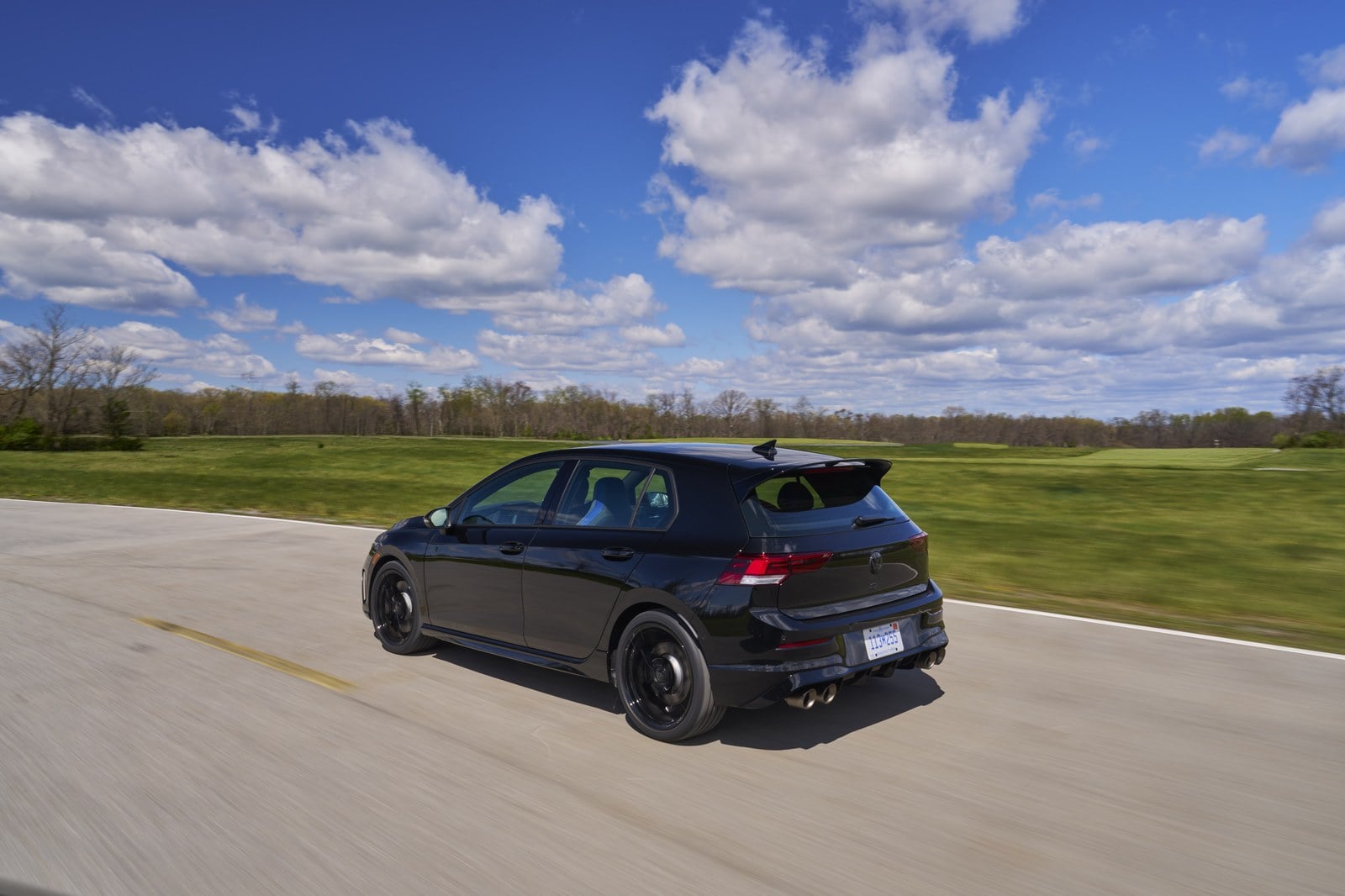 Official Volkswagen photo of a Mythos Black Golf R rear three-quarter driving with quad exhaust tips