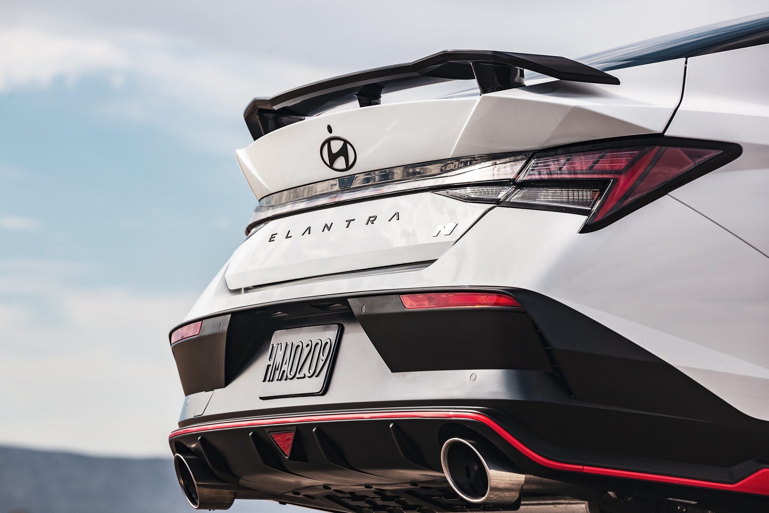 Official Hyundai photo of a white 2026 Elantra N rear three-quarter with wing spoiler and dual exhaust