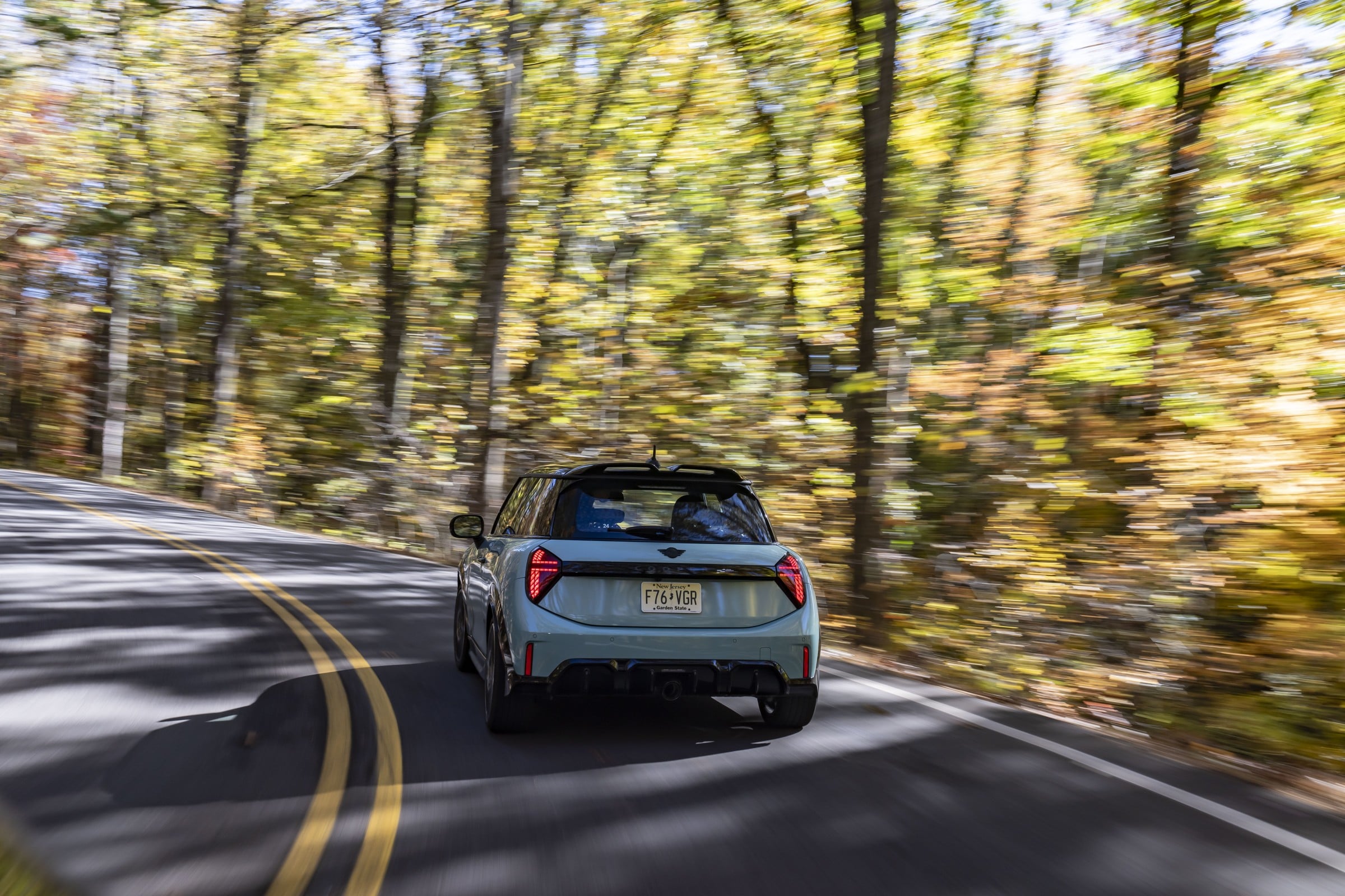 Official MINI photo of a 2027 JCW 2 Door rear three-quarter in motion on a forest road