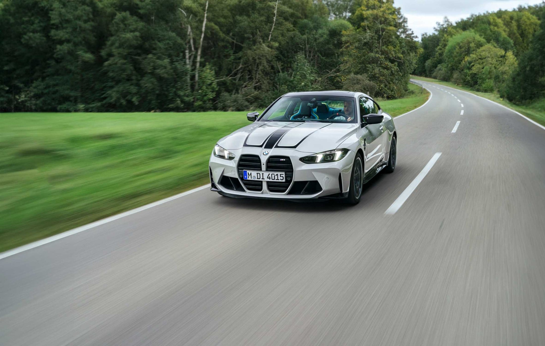 Official BMW photo of a grey M4 Coupe front three-quarter driving on a forest road