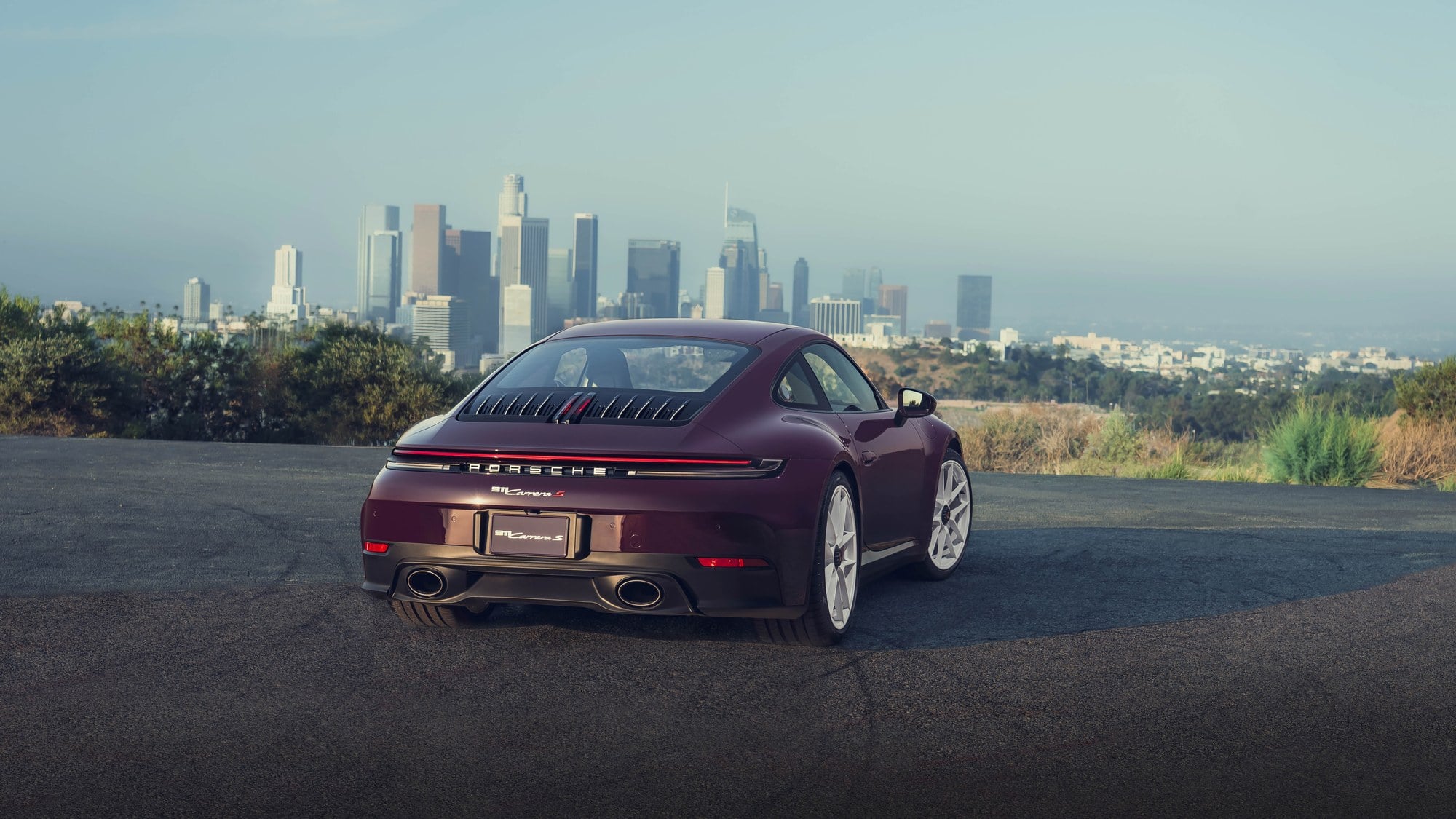 Official Porsche photo of aubergine 2027 911 Carrera S with MT Package rear three-quarter overlooking a city skyline