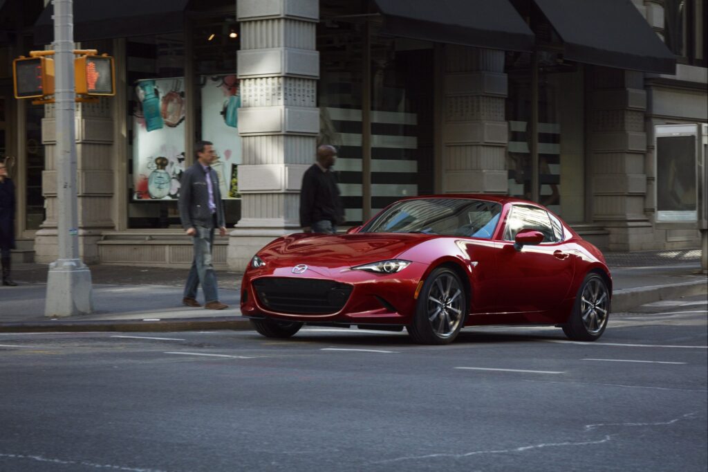 Official Mazda photo of Soul Red Crystal Metallic 2026 MX-5 Miata RF driving through a city intersection