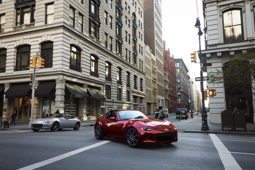 Official Mazda photo of Soul Red Crystal Metallic 2026 MX-5 Miata RF with retractable hardtop open in a city