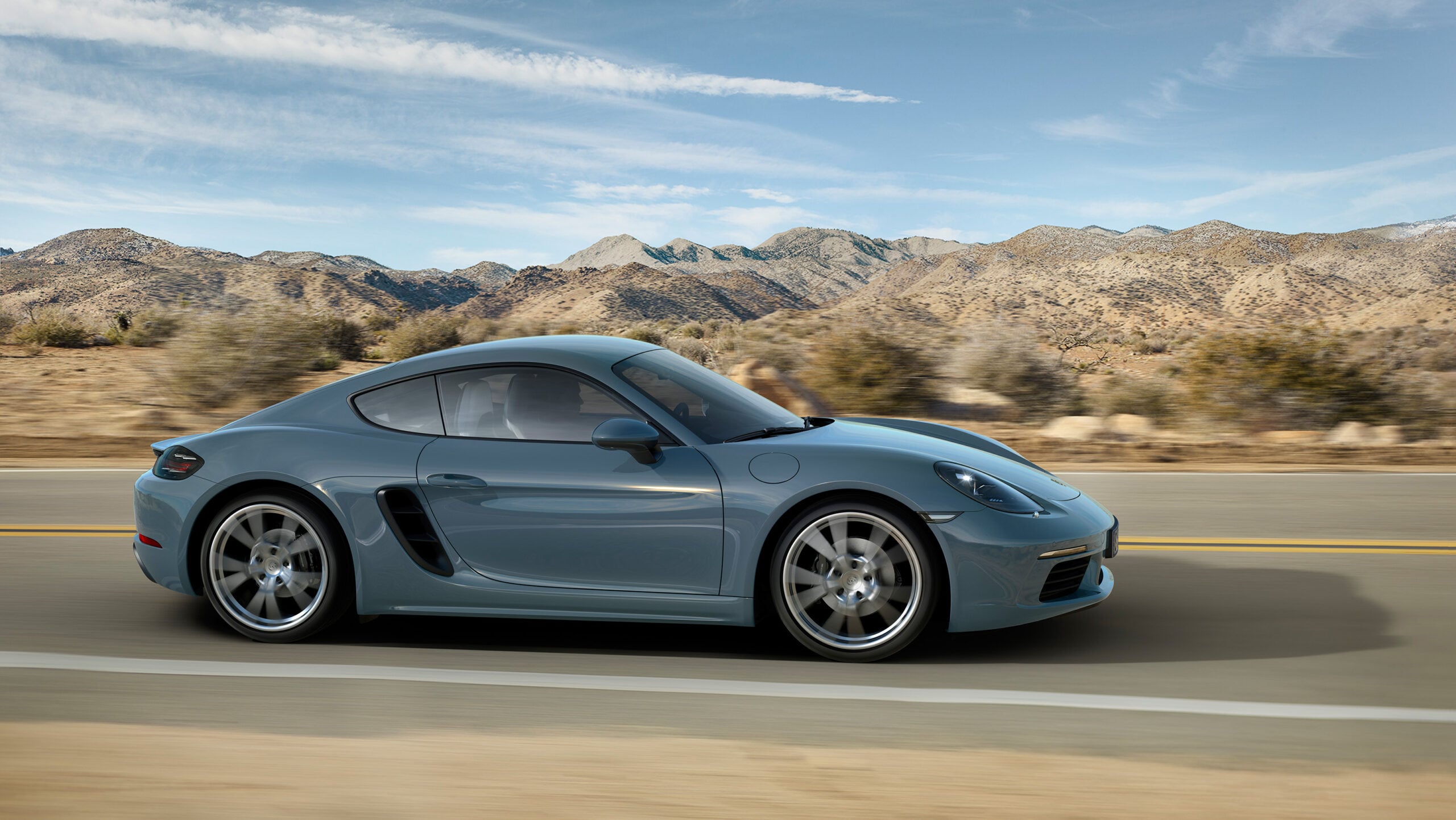 Official Porsche photo of slate 718 Cayman side profile driving on desert highway