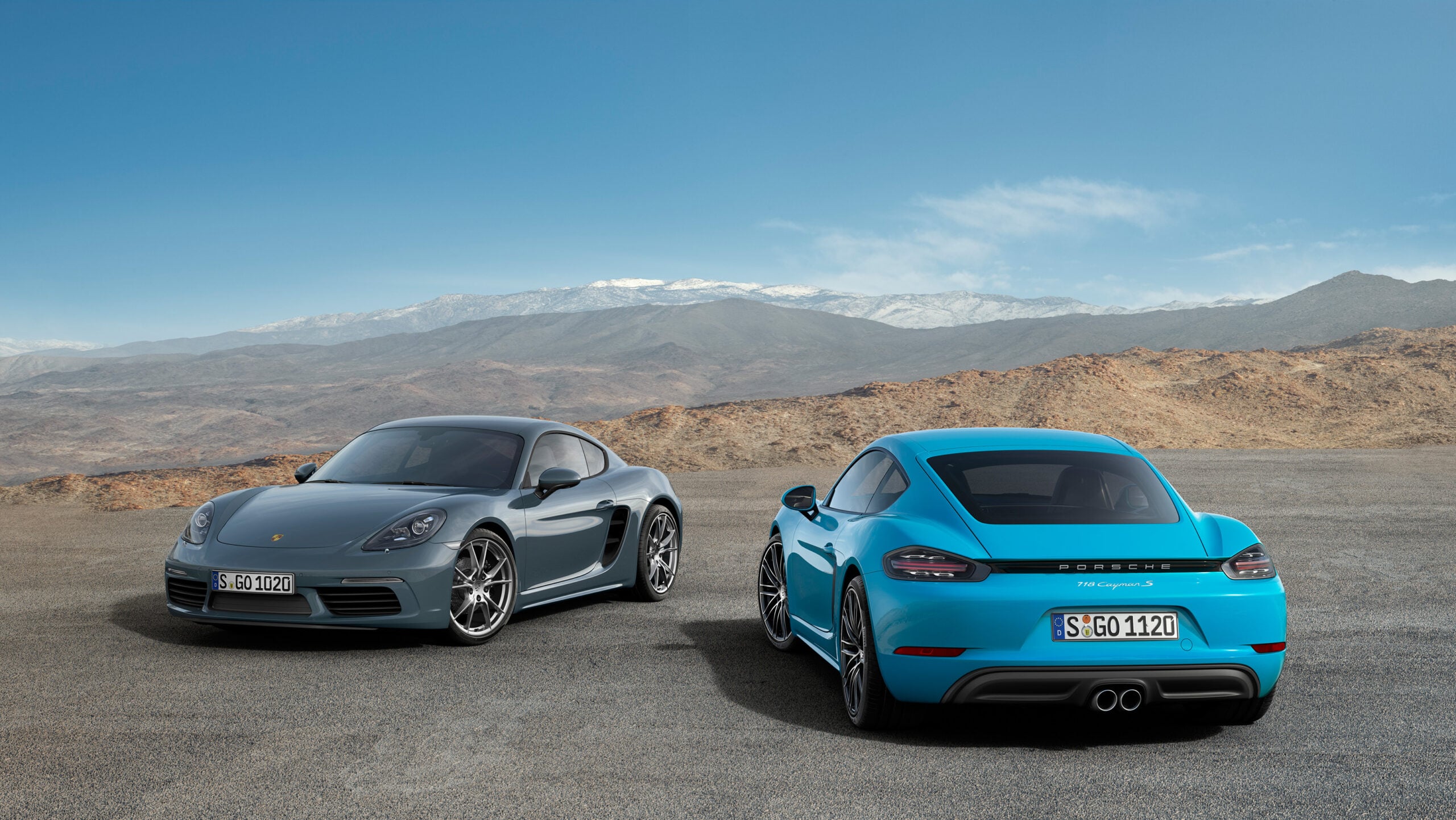 Official Porsche photo of graphite and Miami Blue 718 Caymans parked in mountain landscape