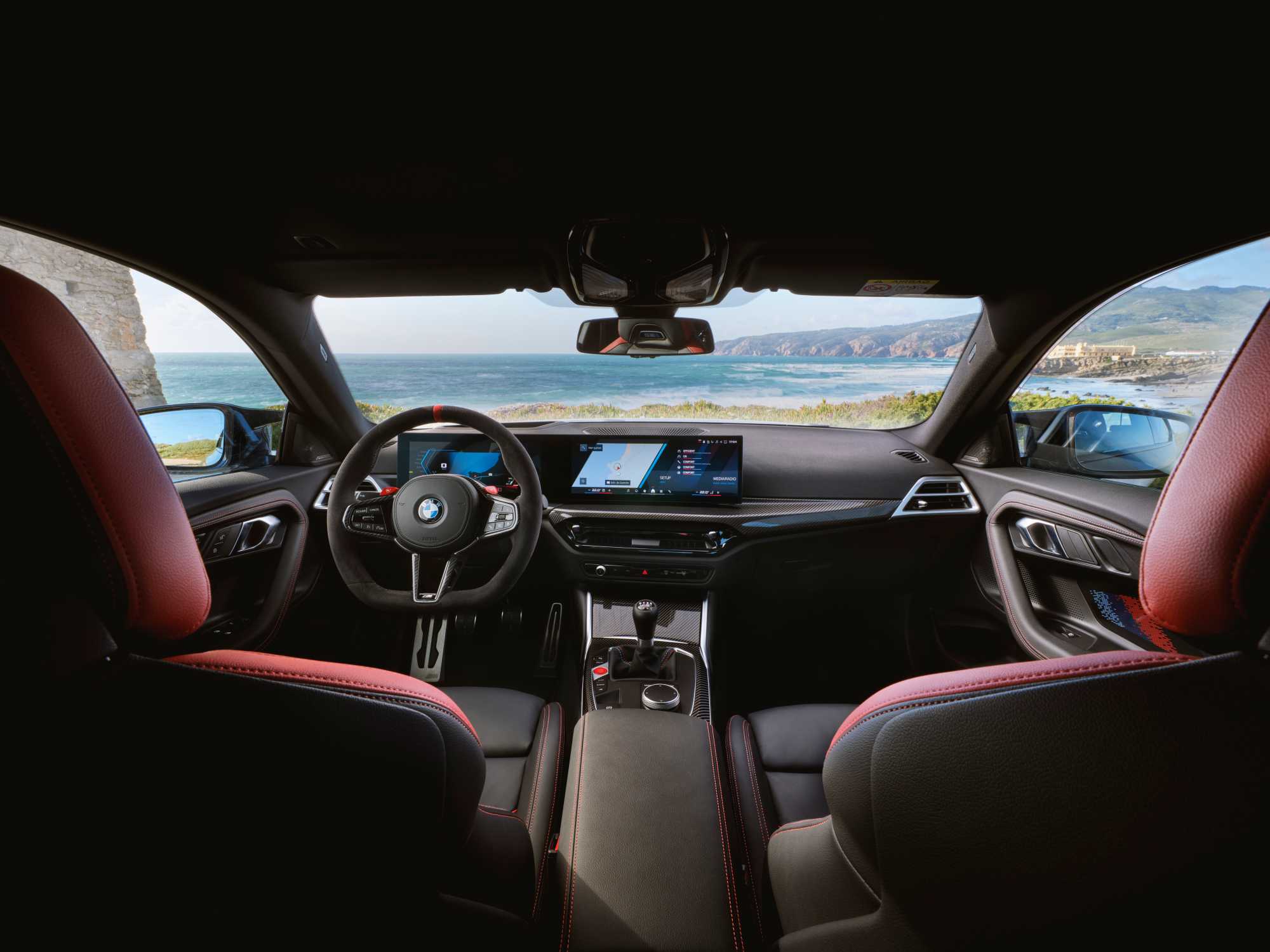 Official BMW photo of BMW M2 cockpit showing Alcantara wheel, curved display, stick, and three pedals