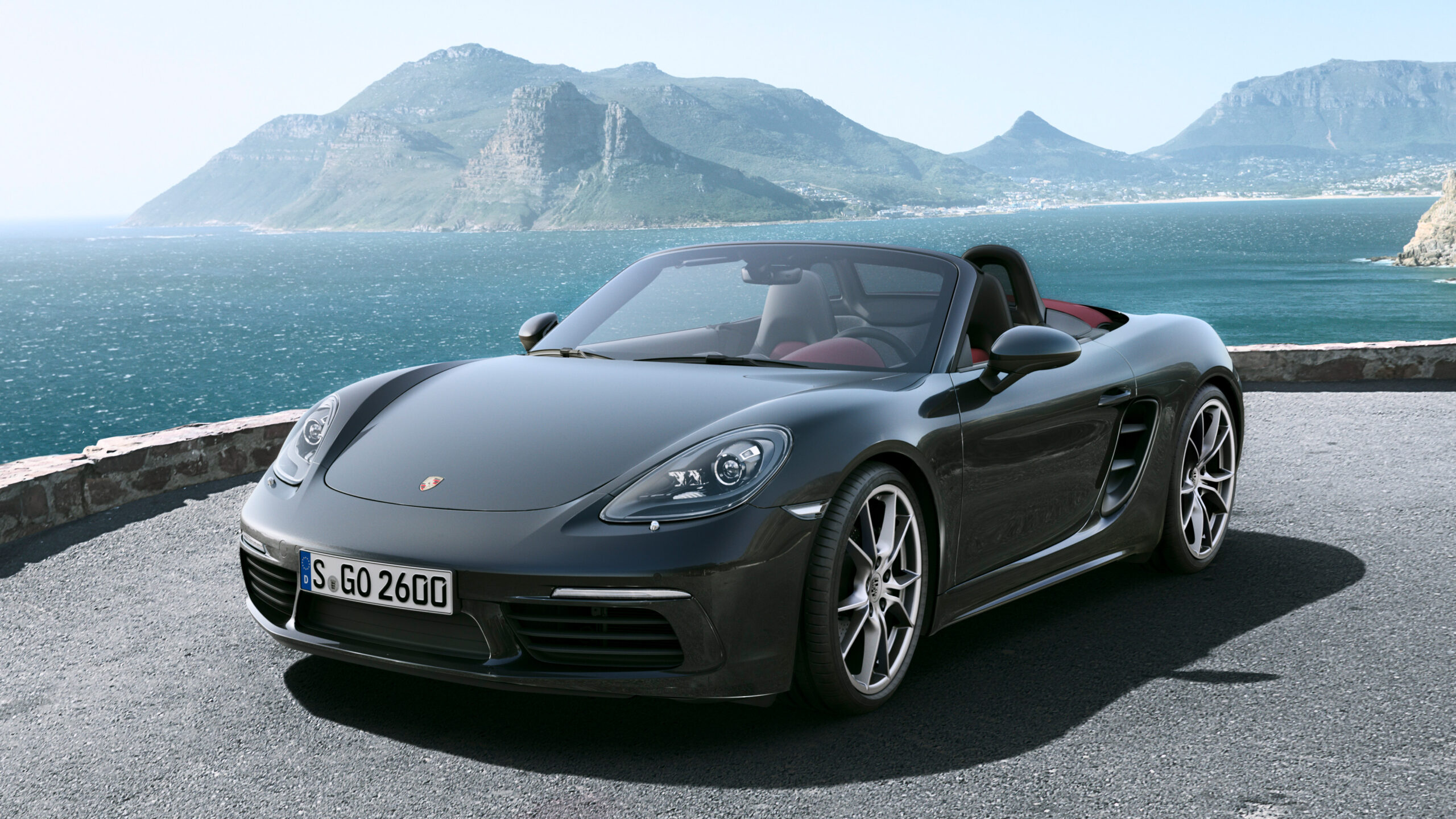 Official Porsche photo of Agate Grey 718 Boxster parked open-top overlooking ocean