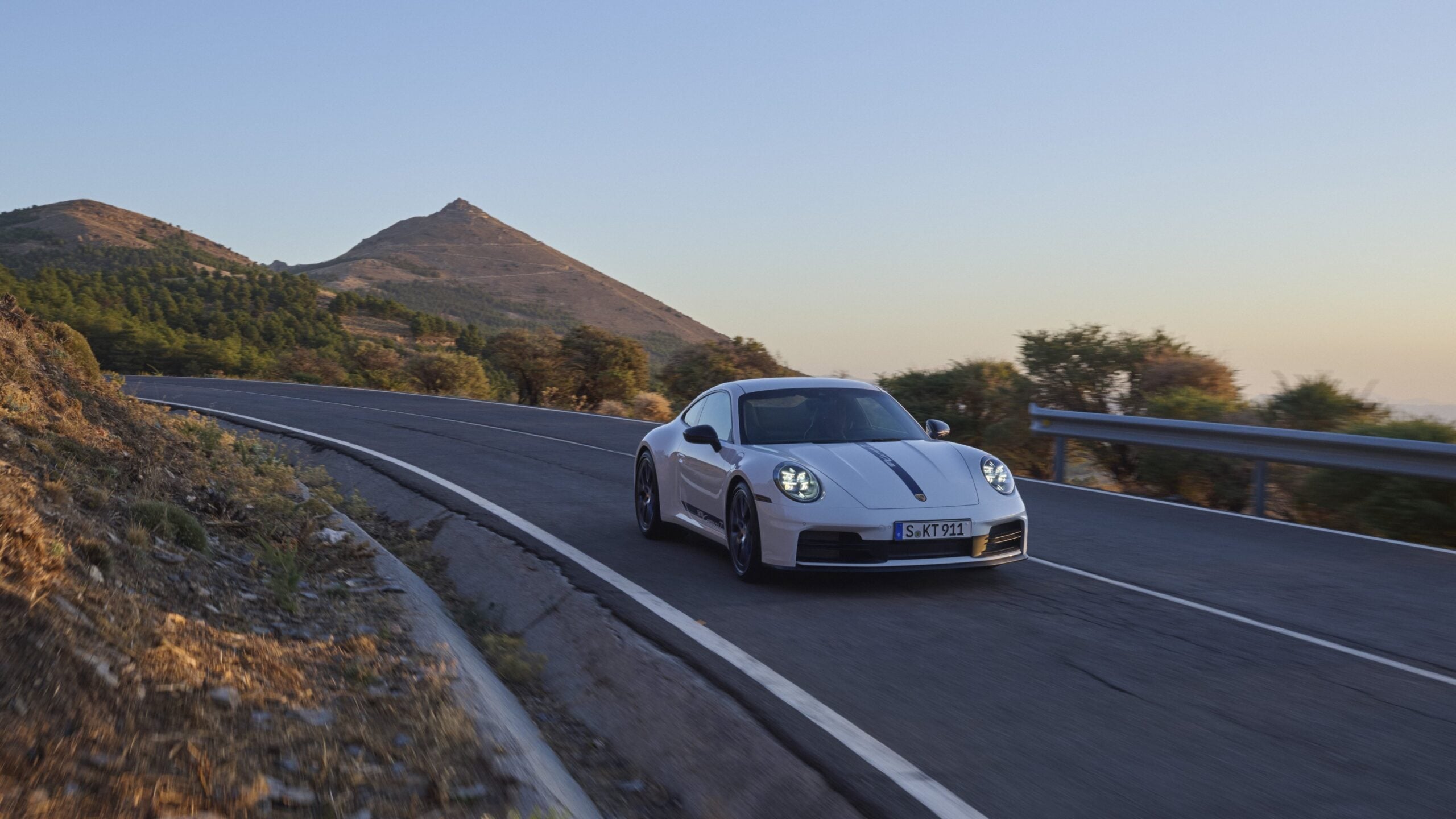 Official Porsche photo of white 2027 911 Carrera T front three-quarter in motion on a mountain road