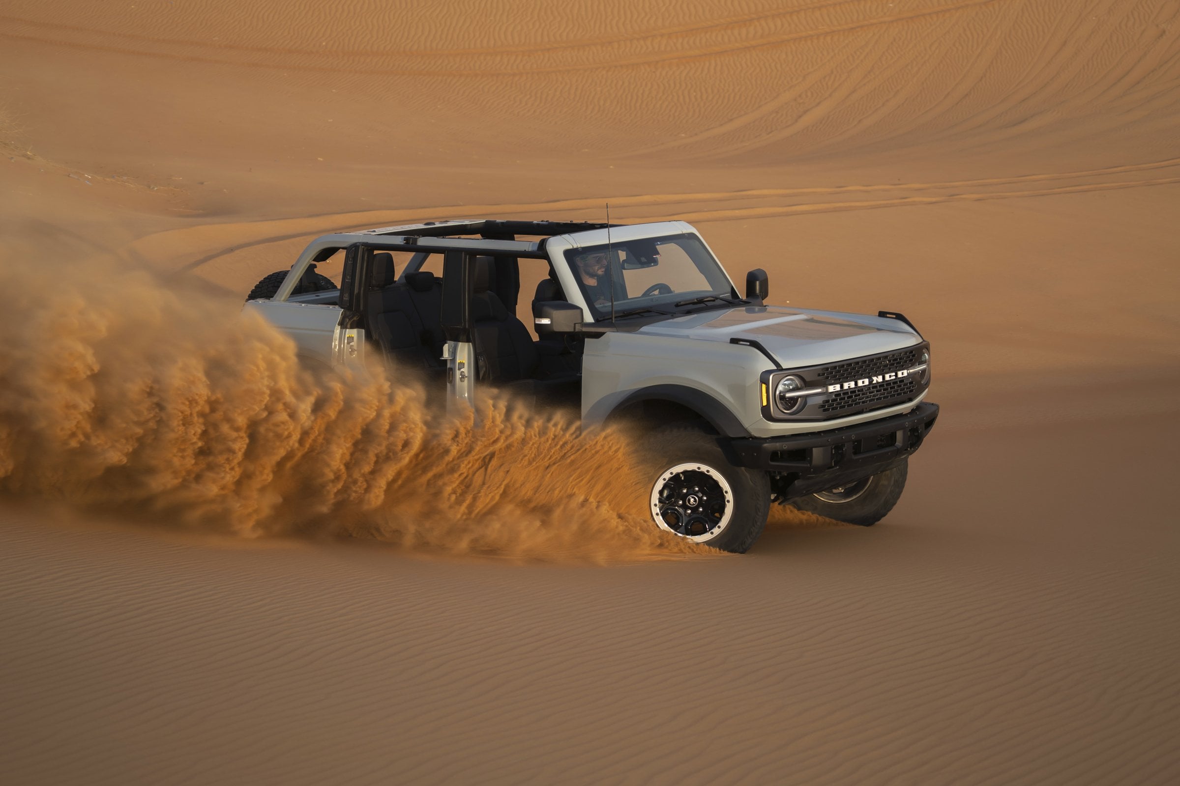 Official Ford press photo of a gray Ford Bronco Badlands with its doors and roof removed, climbing a sand dune