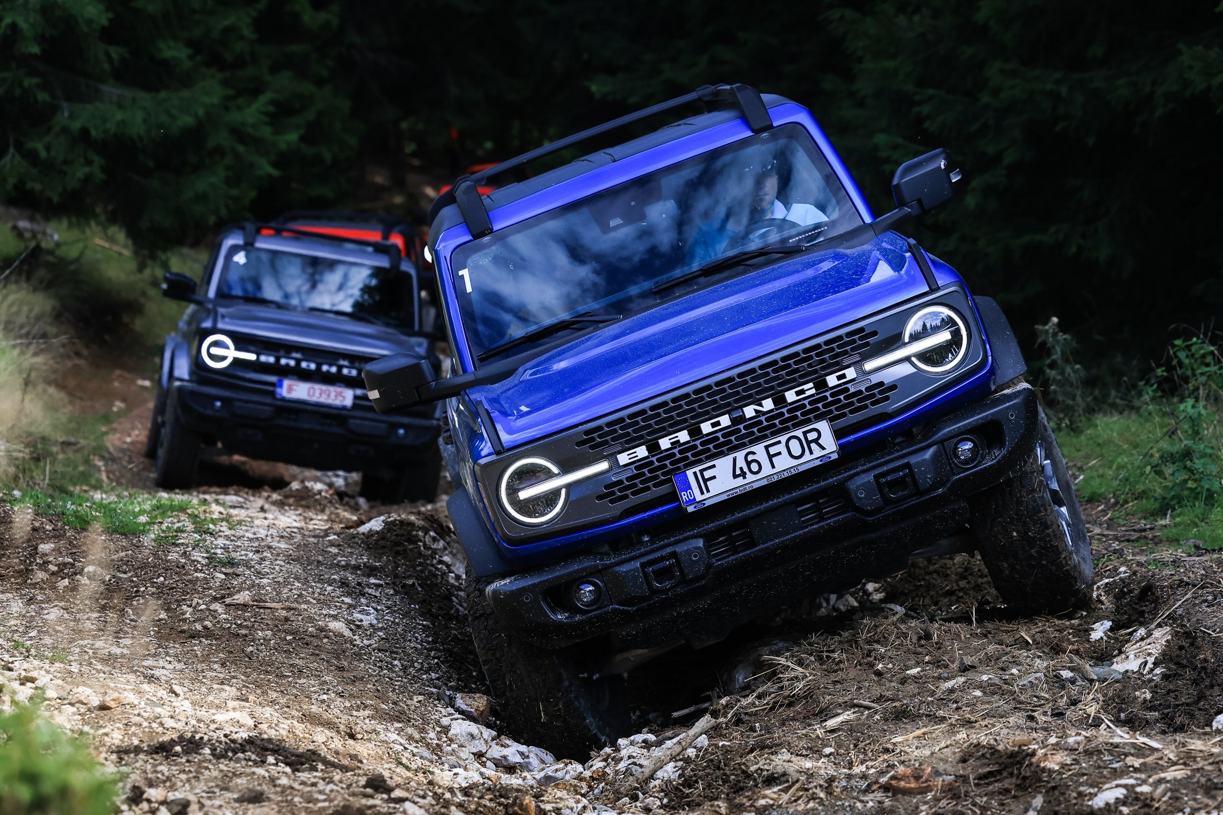 Official Ford press photo of a blue Ford Bronco Badlands crawling a muddy forest trail