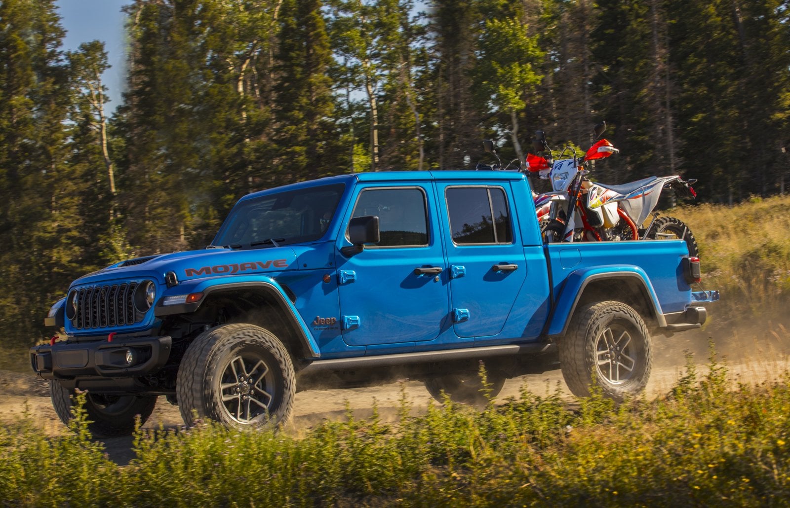 Official Jeep photo of a blue 2026 Jeep Gladiator Mojave X carrying dirt bikes in its steel bed on a mountain trail
