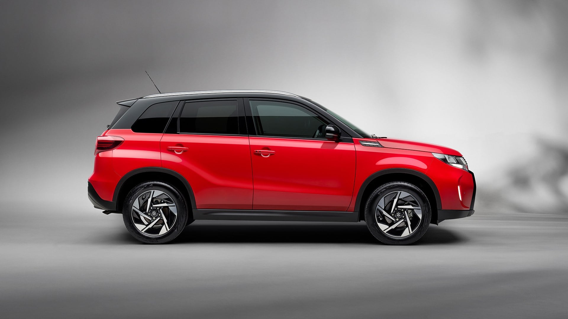 Official Suzuki GB photo of a Bright Red Suzuki Vitara in side profile on a city street