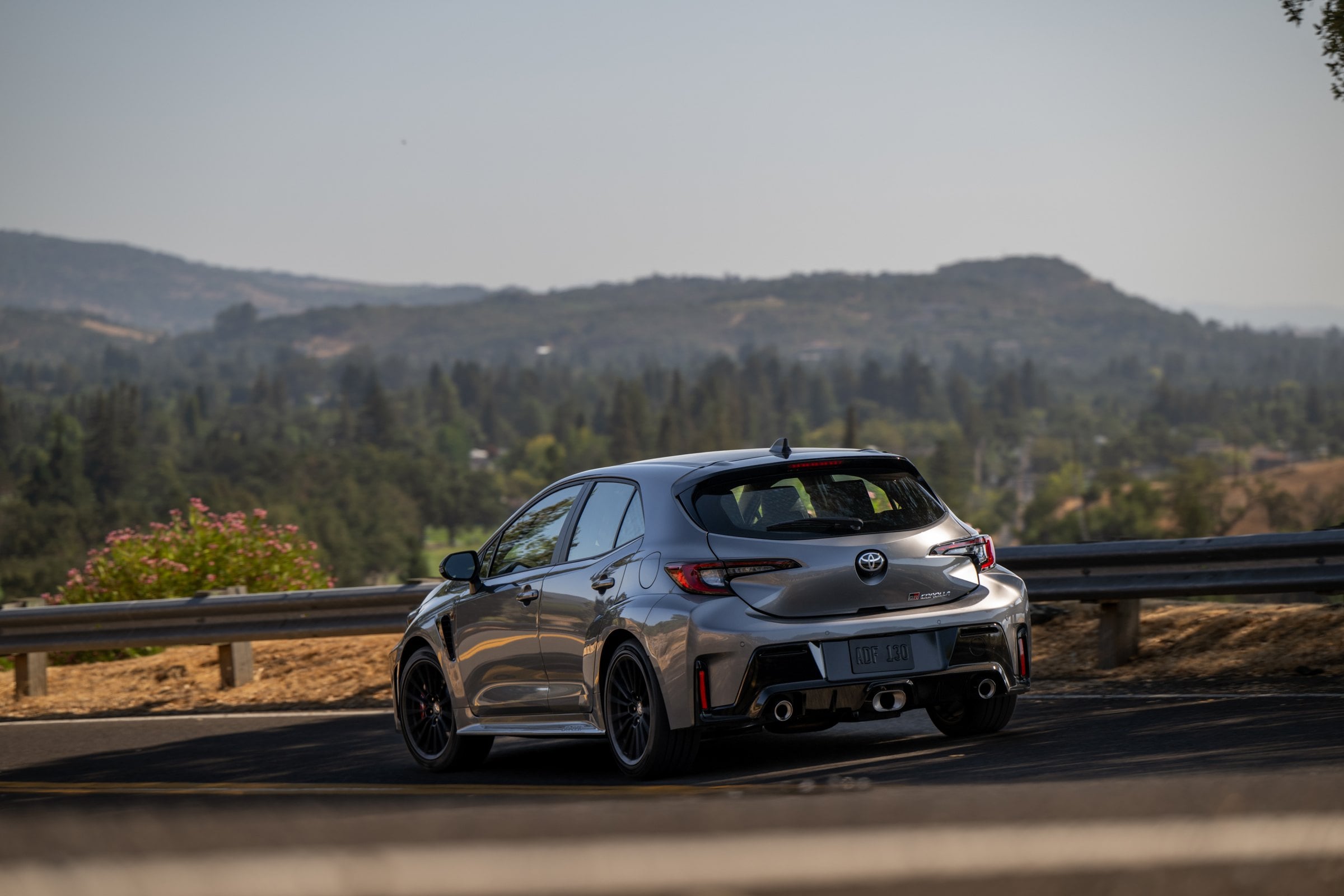 Official Toyota photo of the 2026 GR Corolla Premium Plus in Heavy Metal, rear three-quarter on a canyon road