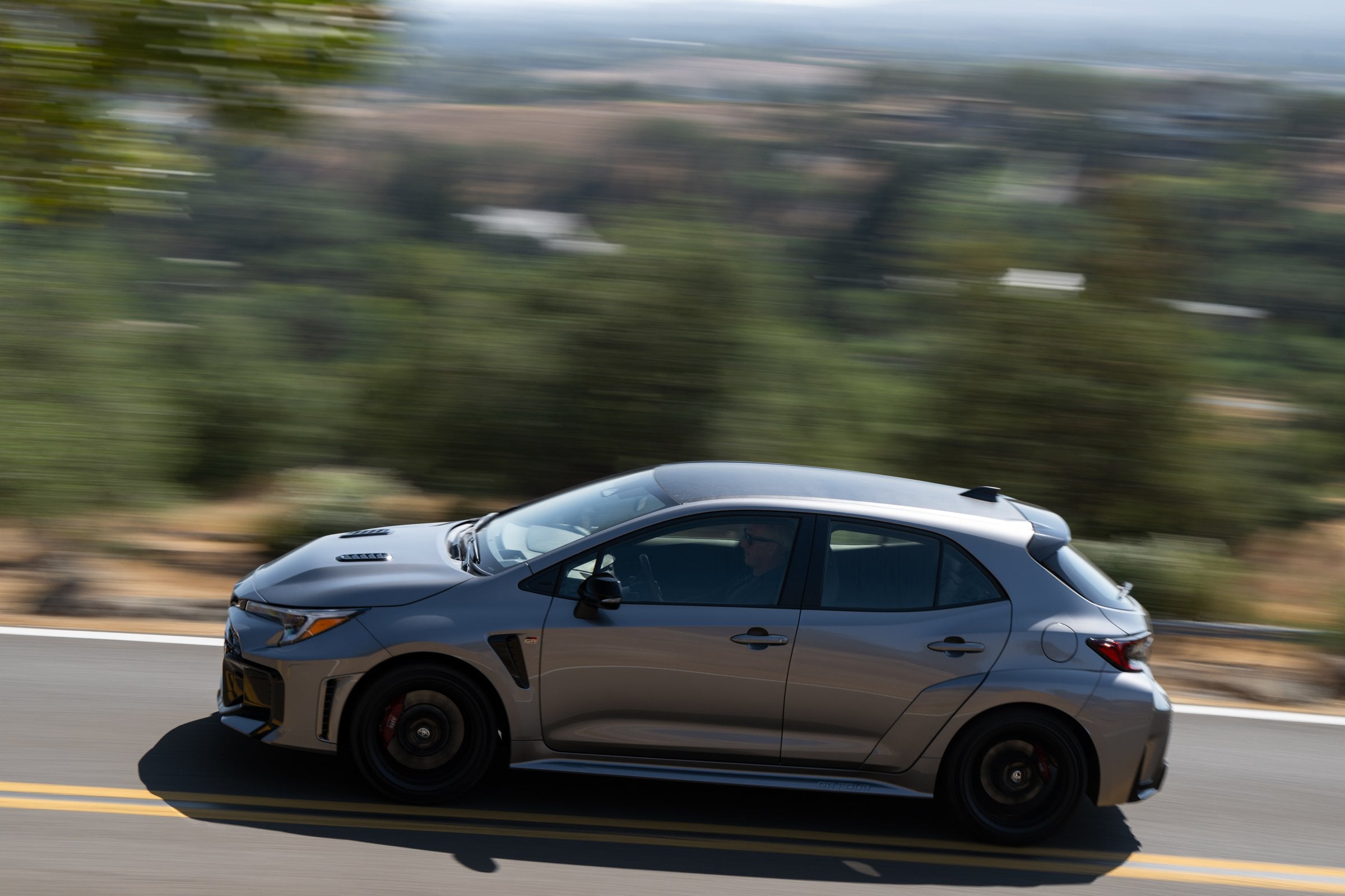 Official Toyota photo of the 2026 GR Corolla Premium Plus in Heavy Metal driving, side profile