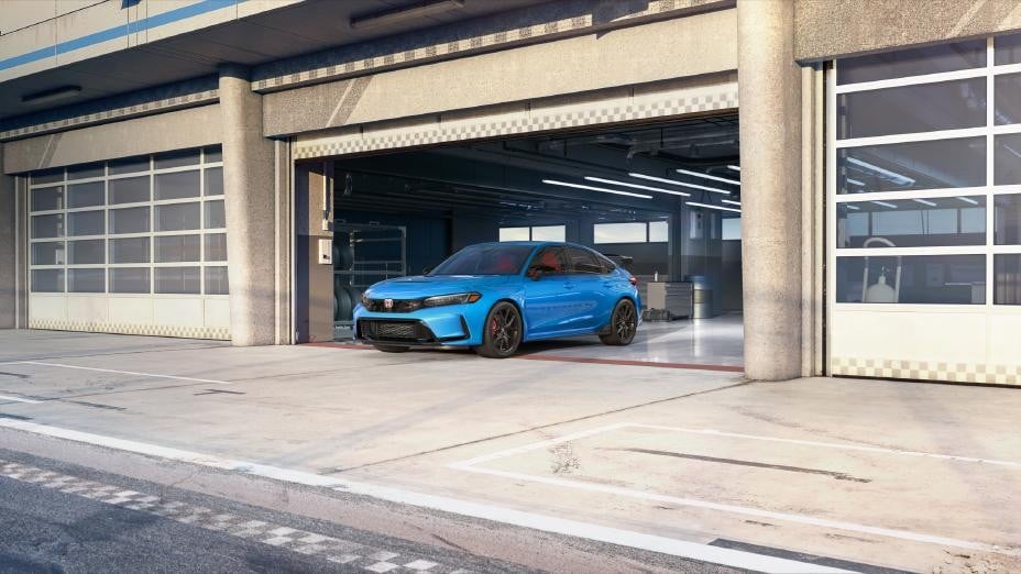 Official Honda photo of a Boost Blue 2027 Civic Type R front three-quarter in a track garage