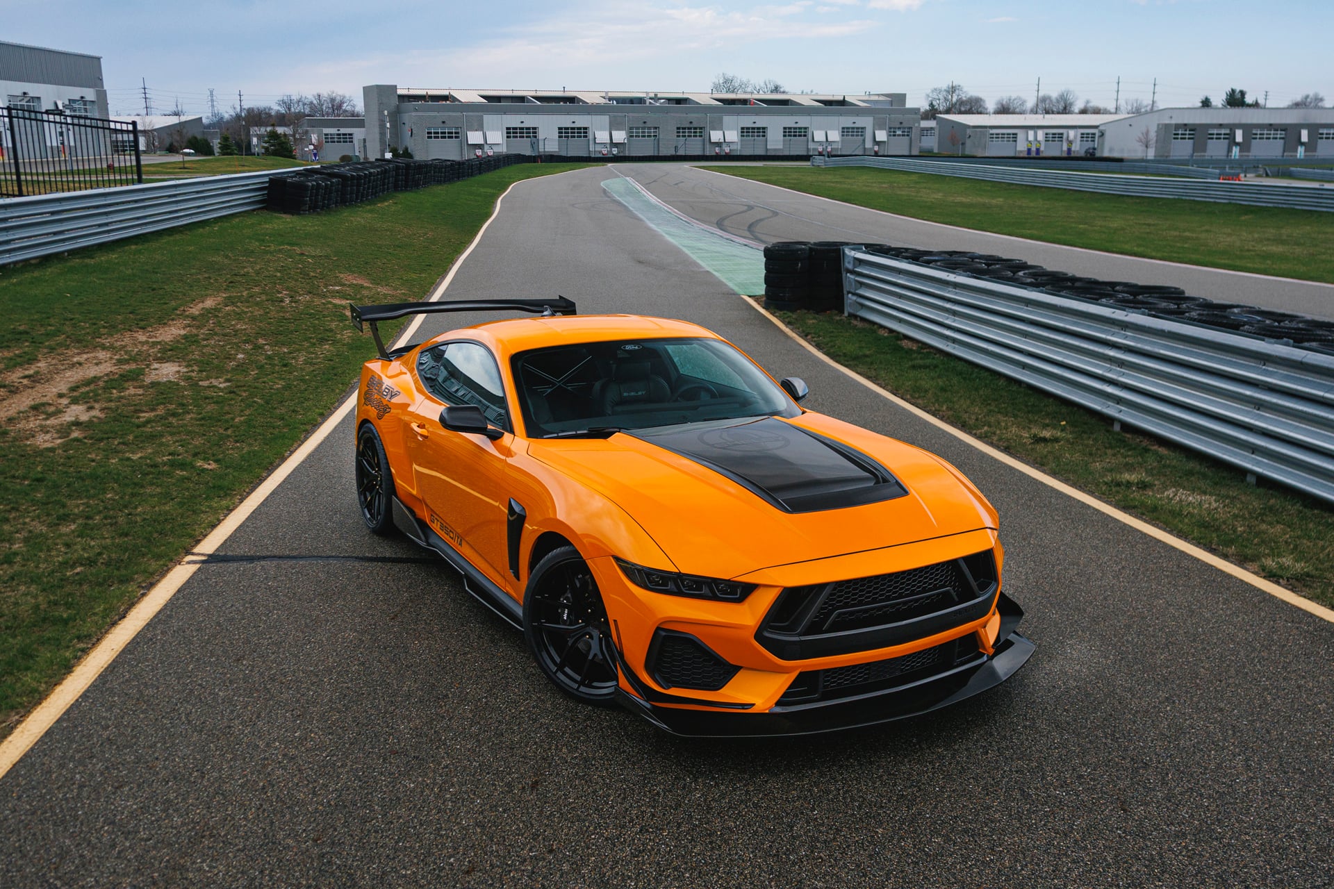 Official Shelby photo of an orange 2026 Shelby GT350/TA high angle showing roll cage and rear wing