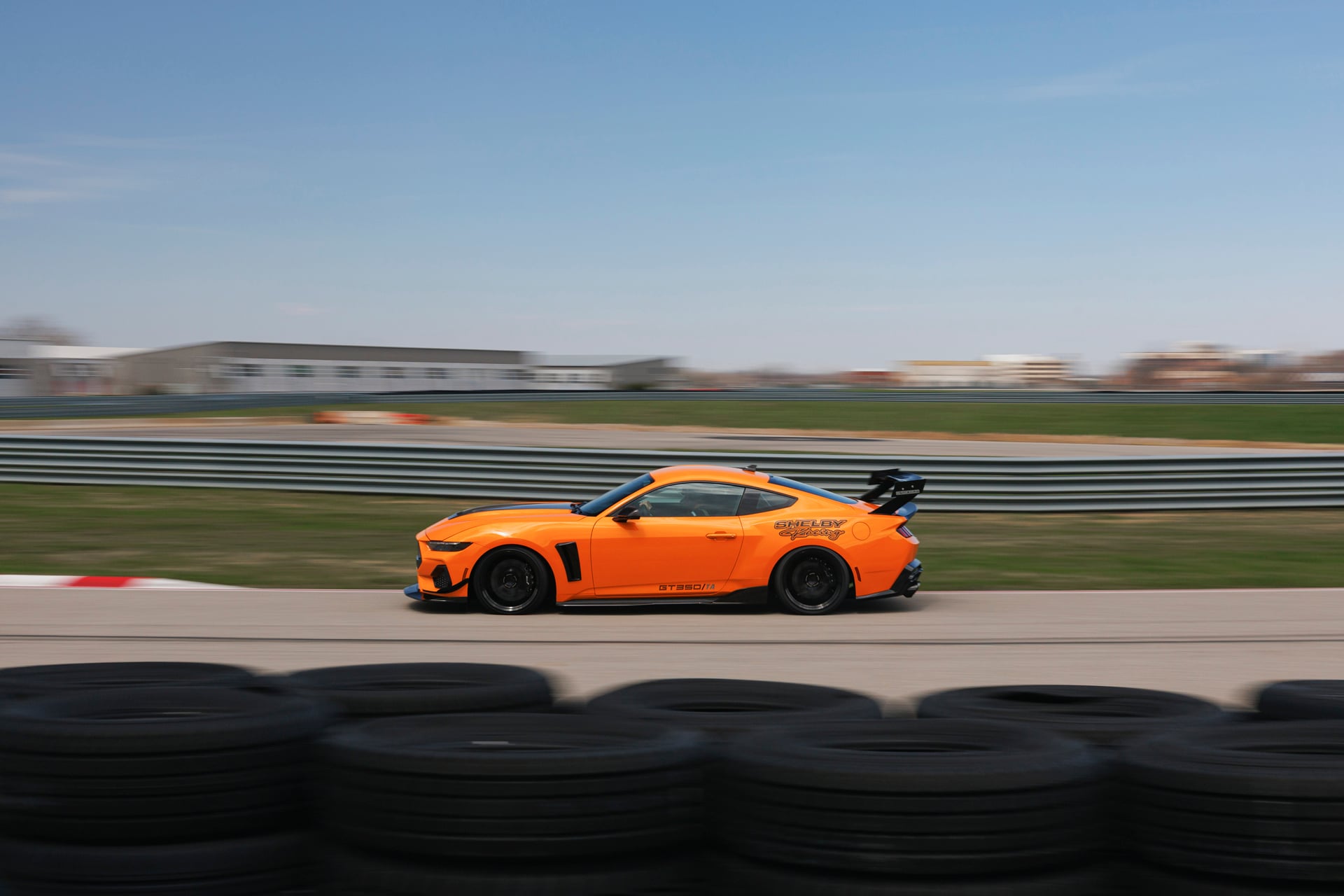 Official Shelby photo of an orange 2026 Shelby GT350/TA side profile at speed