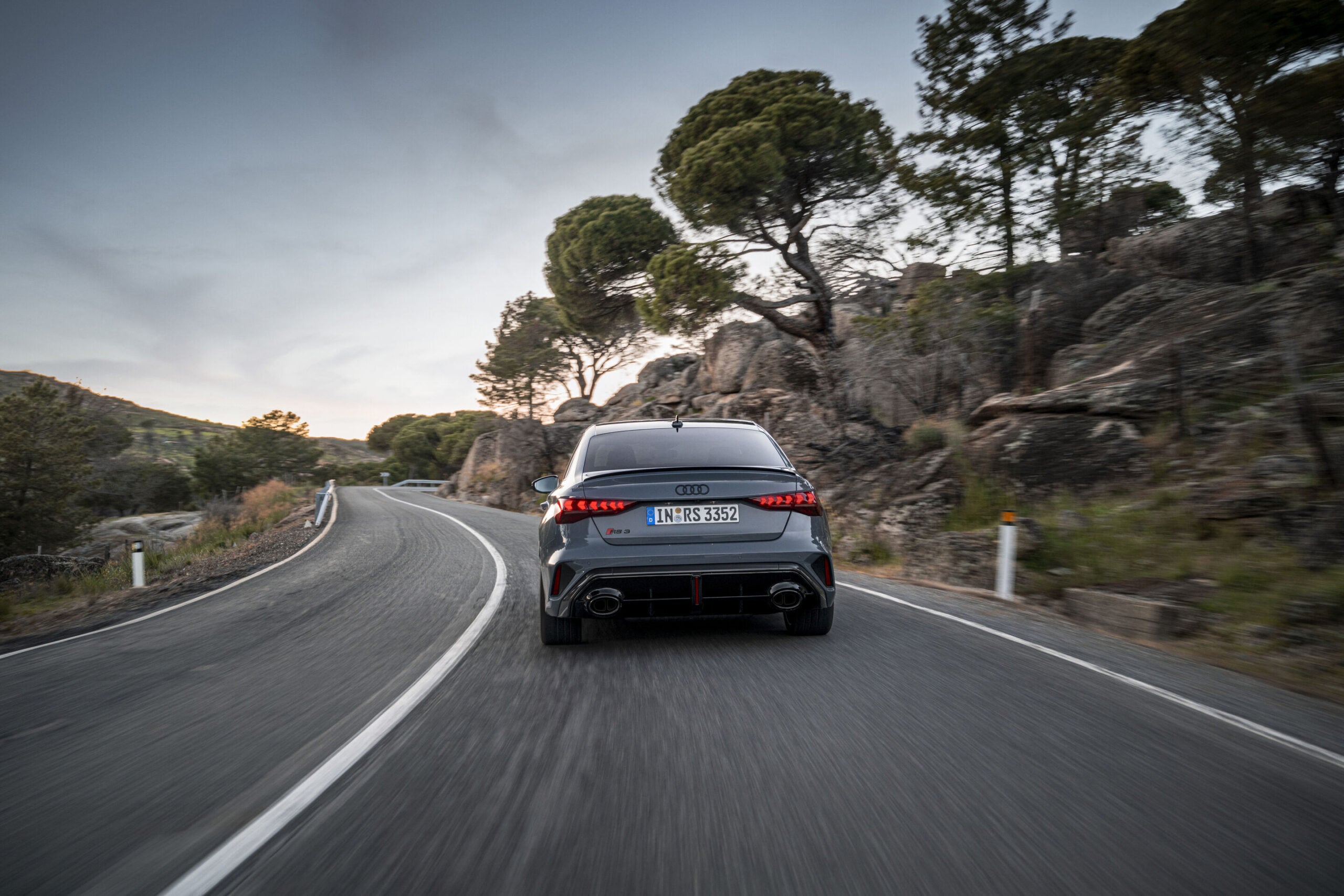 Official Audi photo of a Kemora Gray 2026 Audi RS 3 Sedan rear three-quarter in motion on a winding road