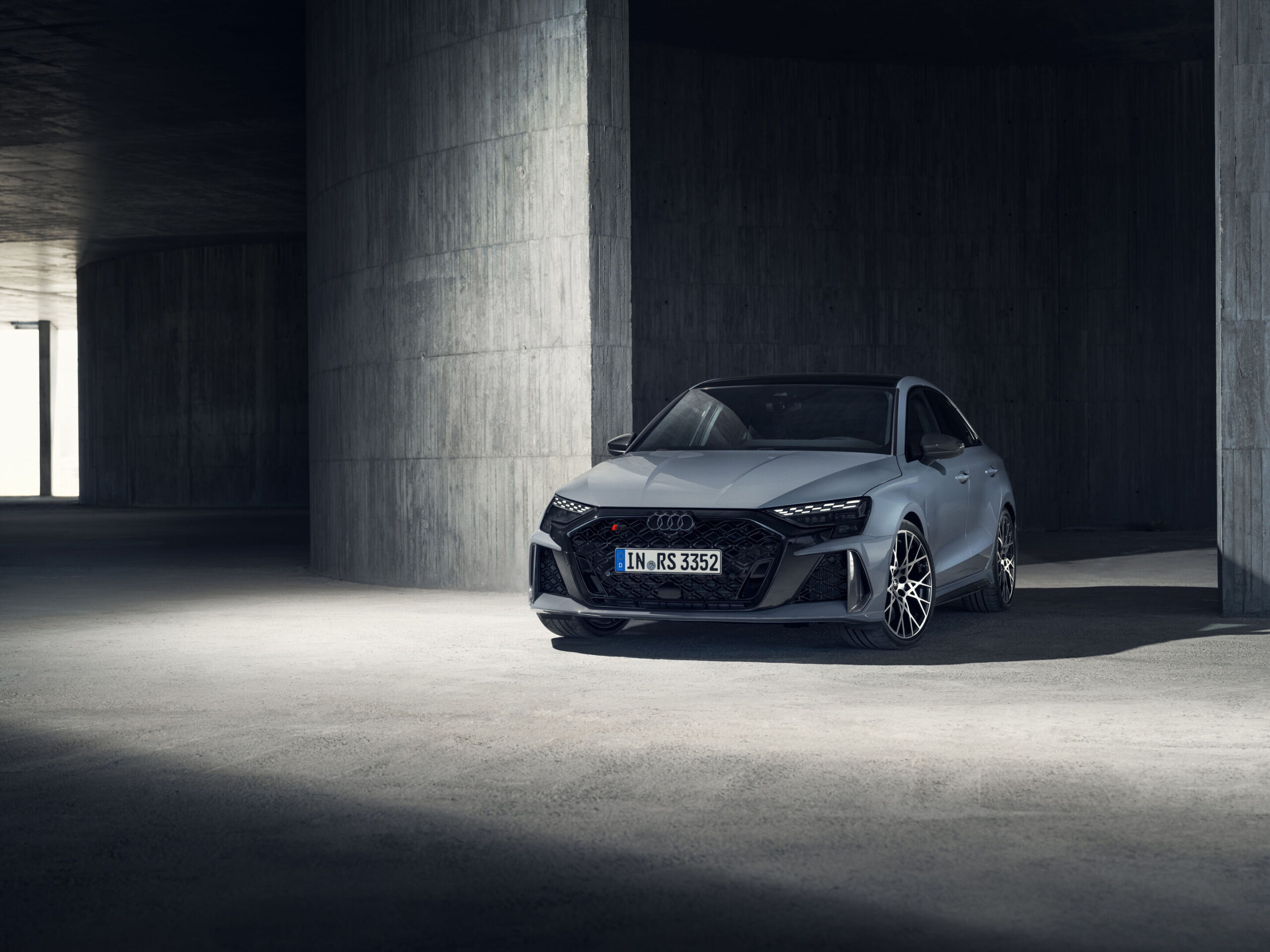 Official Audi photo of a Kemora Gray 2026 Audi RS 3 Sedan front three-quarter in an architectural setting