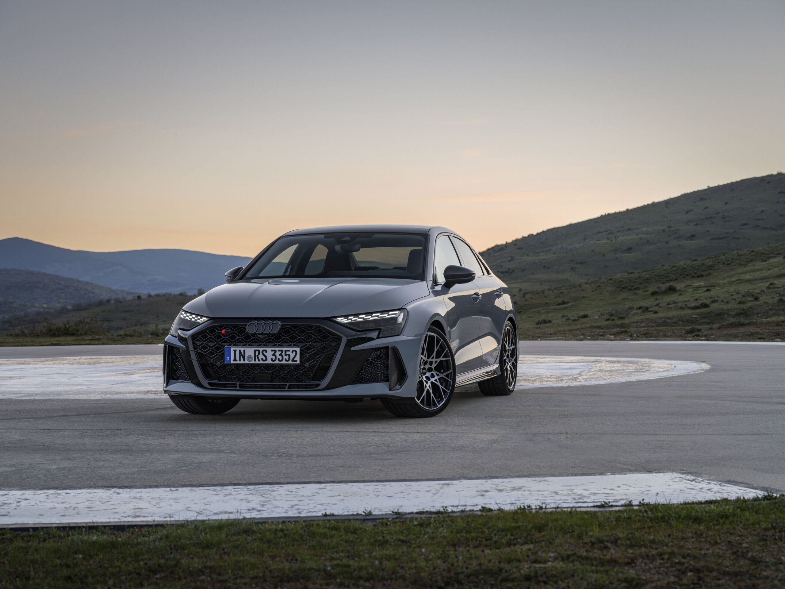 Official Audi photo of a Kemora Gray 2026 Audi RS 3 Sedan front three-quarter at dusk on a mountain pad