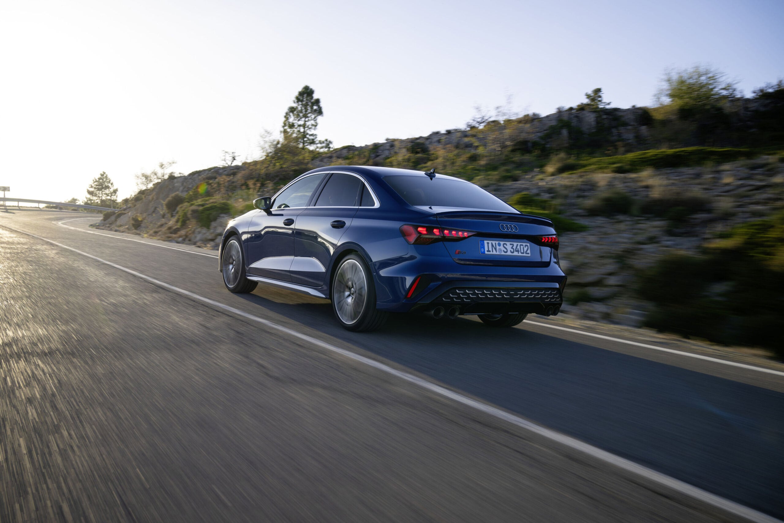 Official Audi photo of a dark blue 2026 Audi S3 rear three-quarter in motion at golden hour